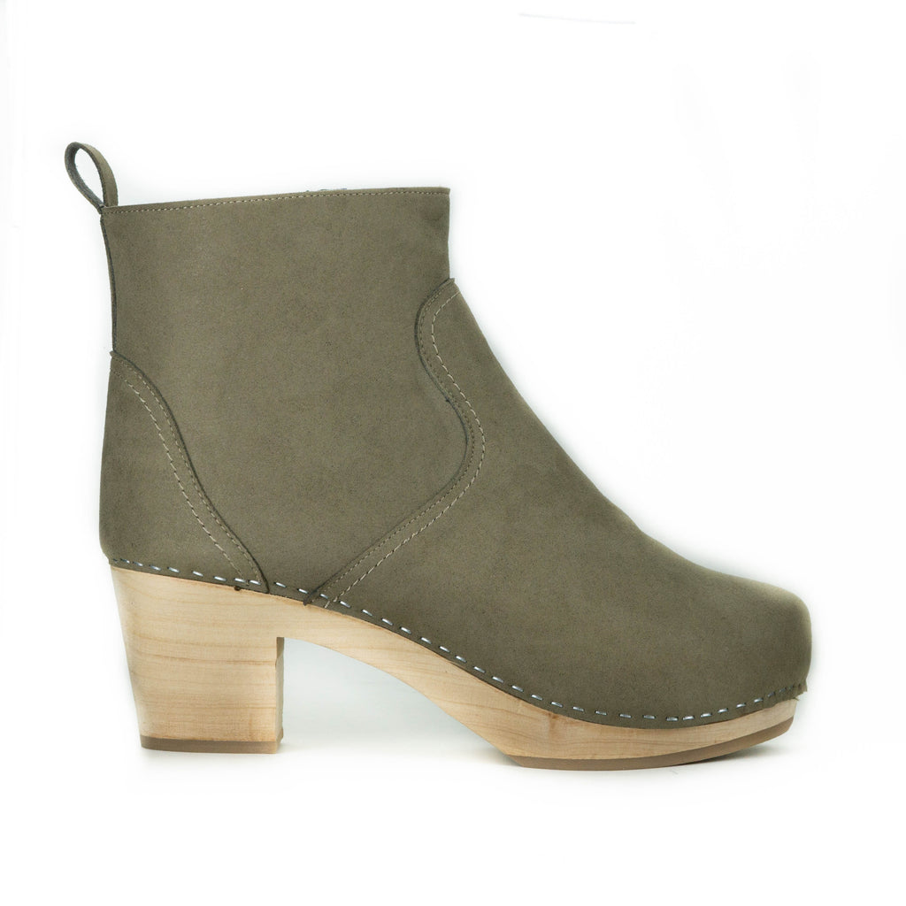 A taupe vegan suede clog bootie. Ankle height shaft with pull tab in back. Inside zipper closure. Blonde wooden sole. Staples around outsole to connect material to sole.