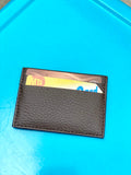 Small cardholder in brown pebbled vegan leather. 2 card slots on each side and slot in middle.  Shown here with a card and Metrocard inside on a blue background.