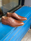 A pair of tan vegan leather men's dress shoes with subtle perforated detailing. Lace up closure with 5 eyelets. Slightly tapered squared toe. Tan sole.